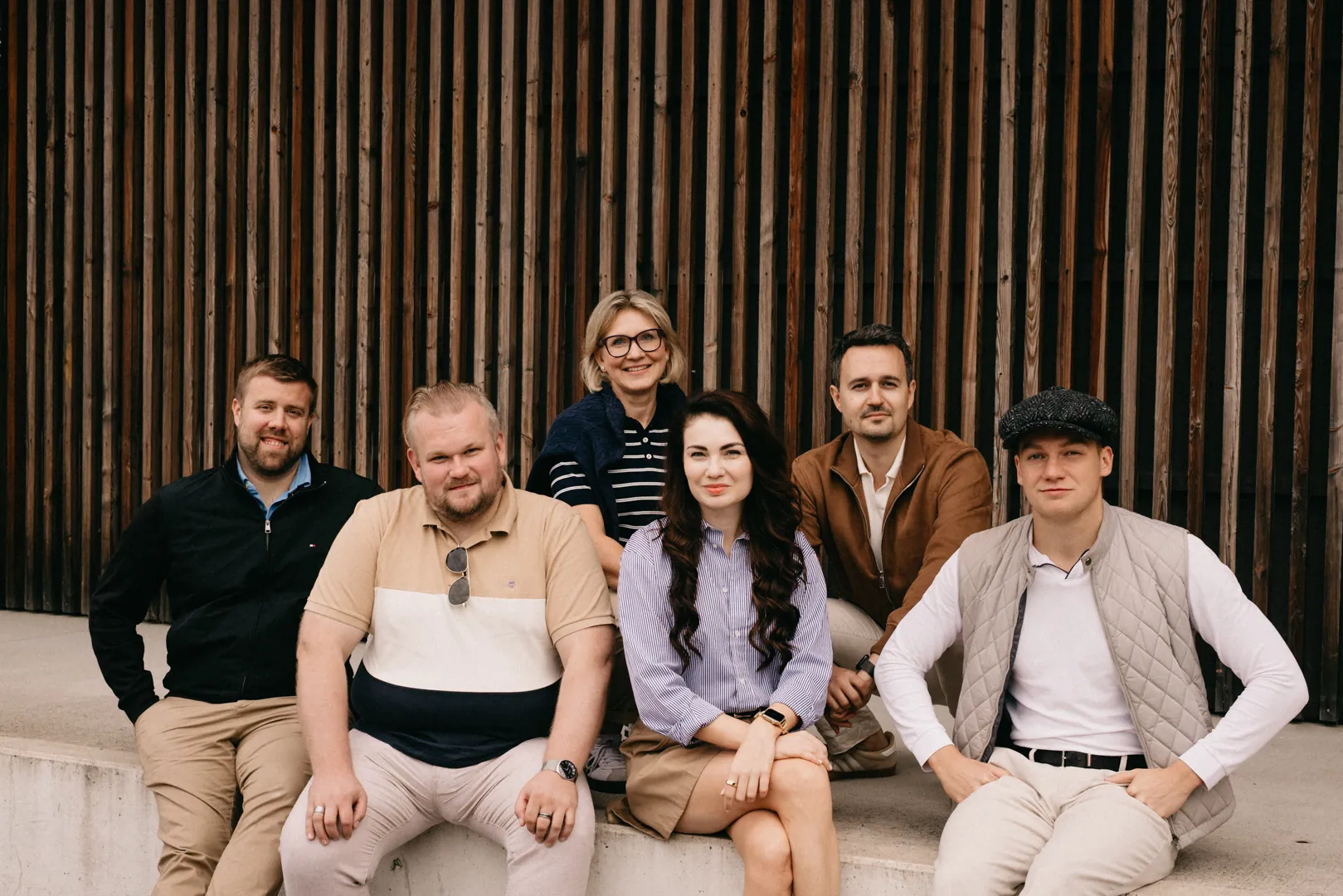 Six WHAT IF team members seated in front of a timber facade